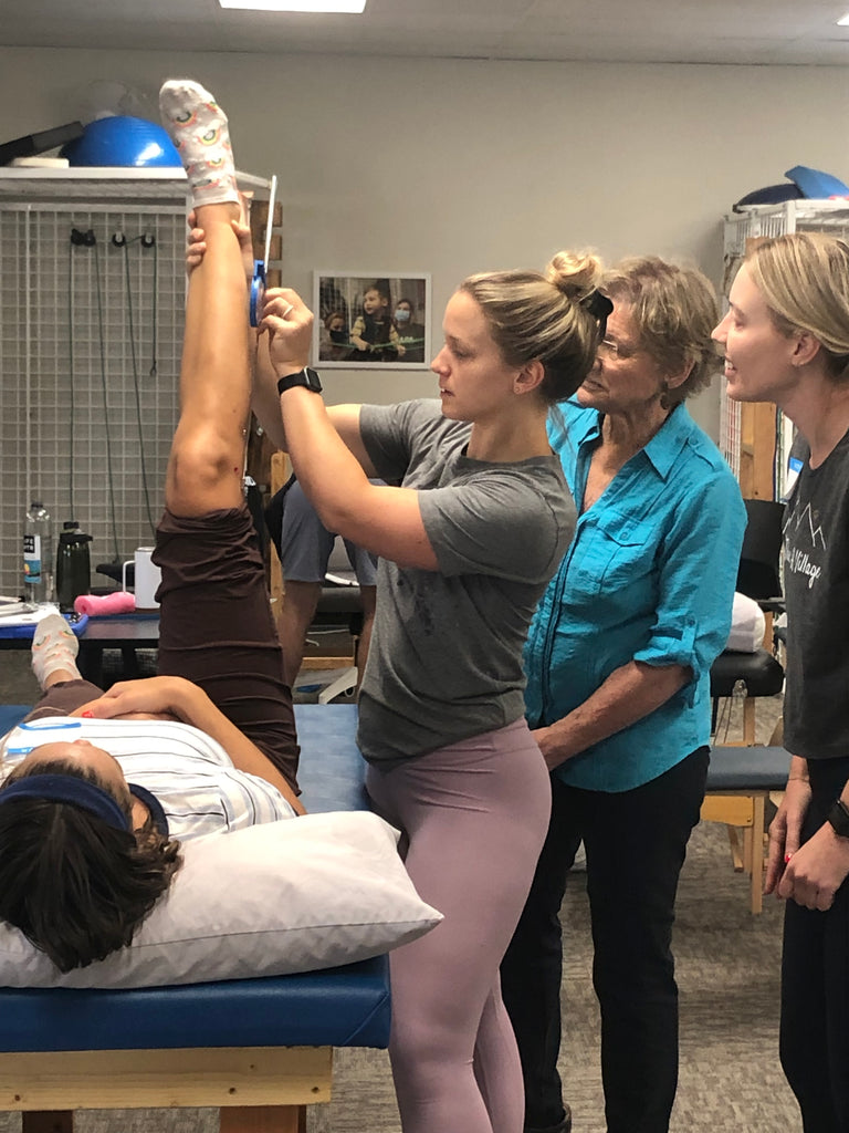 One clinician is taking a lower extremity measurement on another clinician laying supine on a map. Instructor and additional clinician are observing. 