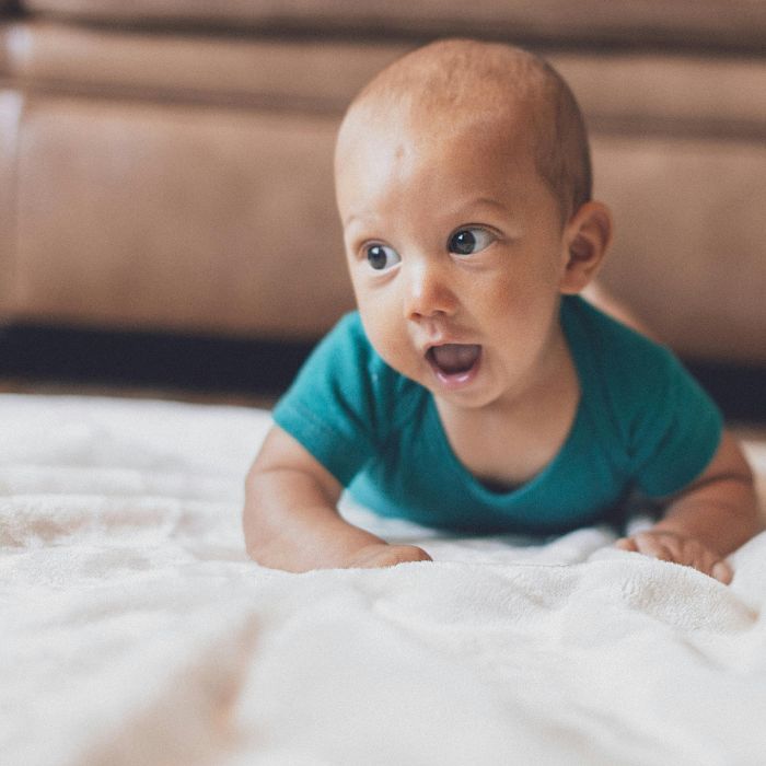 A baby boy is propped on his forearms in tummy time on a ​c​ream blanket with his head lifted and eyes focused ahead. This position illustrates early postural control development, a focus of Progressive GaitWays' Early Postural Control Acquisition course.