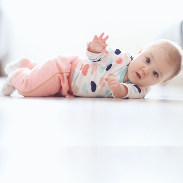 An infant girl, dressed in a colorful heart-patterned outfit, is shown rolling onto her belly, capturing early dynamic movement and postural control. This image relates to Progressive GaitWays' The Golden Rule of Managing Pediatric Orthopedic and Motor Development course.