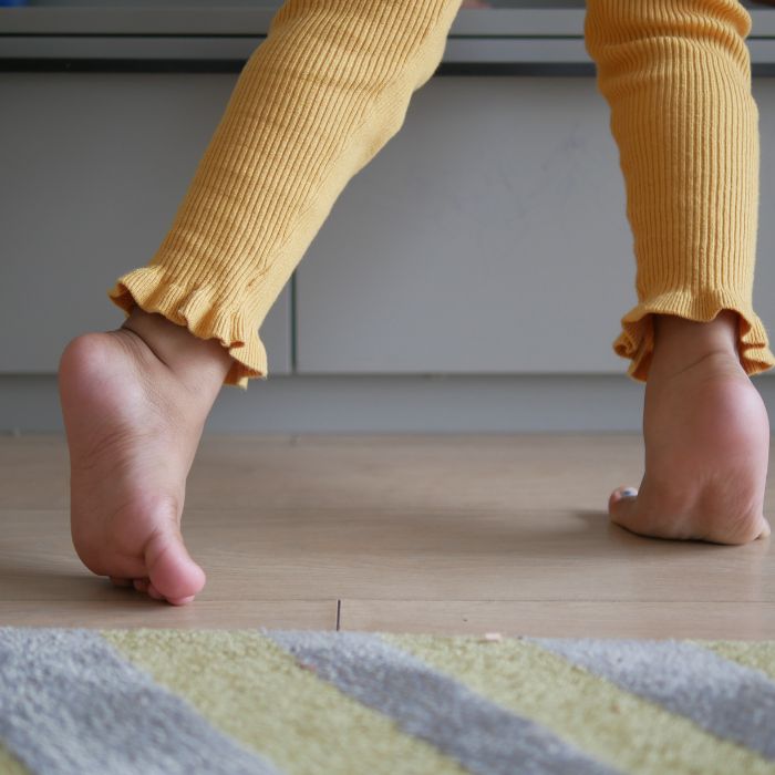 A close-up of a child's foot on tiptoes, wearing mustard-yellow leggings, demonstrating the toe-walking gait pattern often seen in equinus deformity cases, a focus of Progressive GaitWays' training.